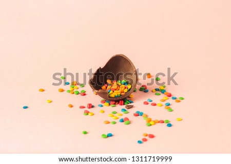 Broken Easter chocolate egg and multi-colored sweets on a pink background. Easter celebration concept.