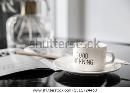 White coffee mug with bouquet of flowers lily of the valley and notes 'good morning' on black modern marble table. Beautiful sunshine morning refreshment.