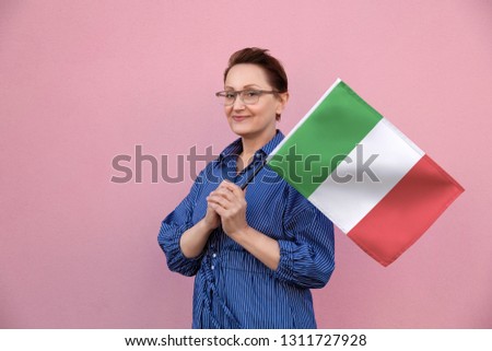 Italy flag. Woman holding Italian flag. Nice portrait of middle aged lady 40 50 years old holding a large flag over pink wall background on the street outdoors.