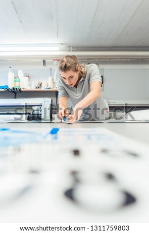 Woman cutting signs or vinyl wraps producing advertising materials in workshop of agency