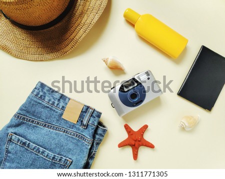 Flat lay summer holidays fashion photo. Top view beach essentials for woman. Sun hat, trendy blue denim shorts, sun hat, camera, passport, yellow sunscreen bottle and seashells. Travel items, baggage
