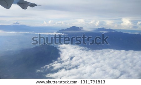 white clouds and blue mountains, viewed from above, picture is taken from airplane window