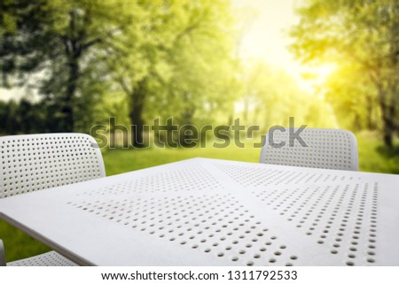 White metal table with two chairs. Free space for your decoration. Spring background of garden and sunny day. 