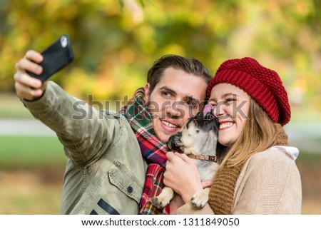 Woman and man with their dog on autumn walk taking a phone selfie