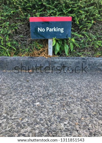 A low wooden No Parking sign posted into the side of the gravel road with green bush background