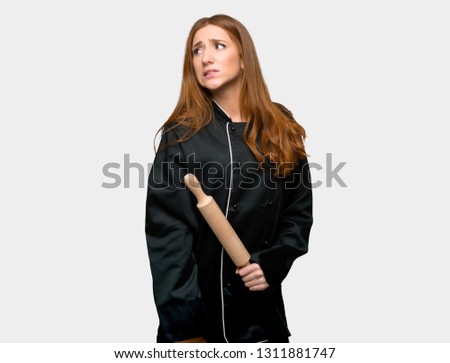 Young redhead chef woman is a little bit nervous and scared pressing the teeth on isolated grey background