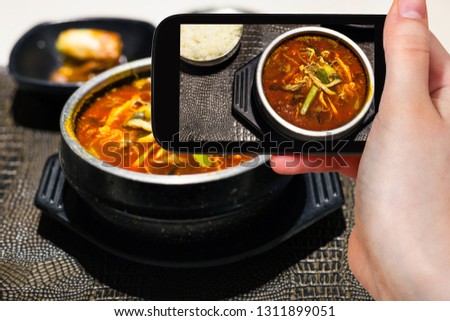 travel concept - visitor photographs of korean cuisine of yukgaejang (spicy soup with beef, eggs, mushrooms, starch noodles, scallions, ferns, bean sprouts, served with boiled rice) on smartphone