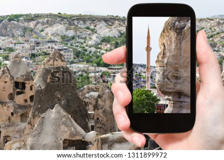 travel concept - tourist photographs of wall of ancient rock-cut house and mosque in Goreme town in Cappadocia on smartphone in Turkey in spring