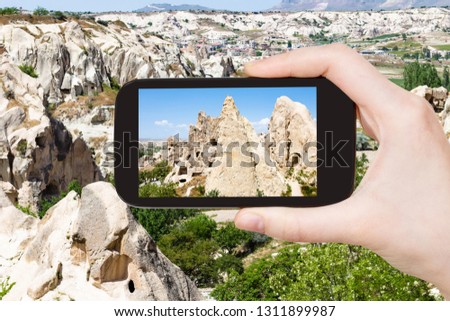 travel concept - tourist photographs of ancient rock-cut monastic settlement near Goreme town in Cappadocia on smartphone in Turkey in spring