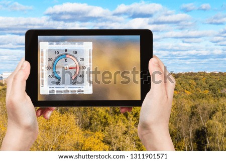 travel concept - tourist photographs city park and outdoor thermometer on home window in hot autumn day on smartphone in Moscow, Russia