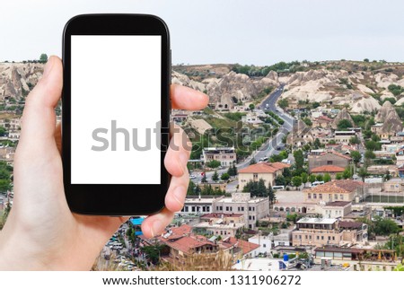 travel concept - tourist photographs of road in modern residential district in Goreme town in spring in Turkey on smartphone with empty cutout screen with blank place for advertising