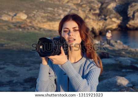 A woman holds in her hand a camera with a big lens and the mountains in the background