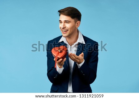 Cute young man in a white shirt and blue jacket holding a box with a gift am