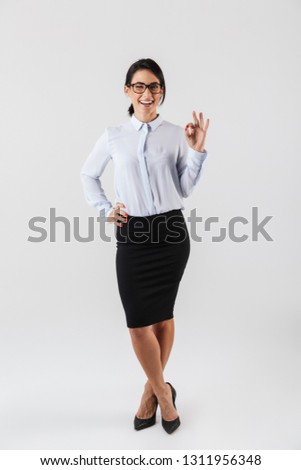 Full length photo of caucasian businesswoman wearing eyeglasses standing in the office isolated over white background