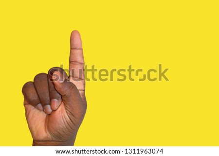 Hand finger pointing up, isolated on a yellow background. Raised hand asking for permission or answering a question. Inclusion and participation concept. African person's hand.