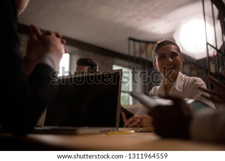 Bottom View Of A Smiling Businesswoman At Office Meeting. Dark Image Of Beautiful Female Holds Her Phone And Smiles At Business Meeting During Negotiations.