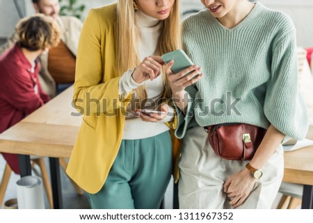casual businesswomen using smartphones in loft office with colleagues on background