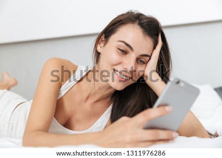 Beautiful young woman relaxing on bed at home, using mobile phone