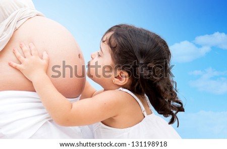 Cute litte girl kissing mums belly outdoors