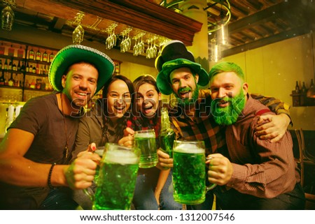 Saint Patrick's Day Party. Happy friends is celebrating and drinking green beer. Young men and women wearing a green hats. Pub Interior.
