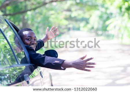 African business man driving and  smiling while sitting in a car with open front window.