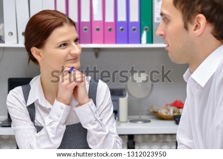 Concept portrait of a pretty brunette manager girl in an office at the table discussing a project and talking with a client. They are right in front of the camera and listen to each other.