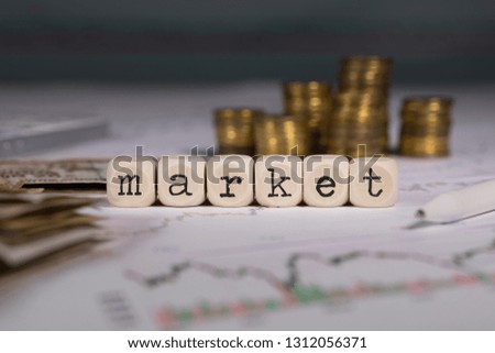 Word MARKET composed of wooden letter. Stacks of coins in the background. Closeup
