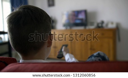 boy sits on the sofa in front of the TV and switches the channels