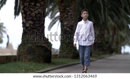 funny boy walk on the road against the backdrop of palm trees, looking up