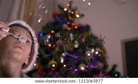 boy in a Santa Claus hat blowing soap bubbles on the background of a New Year tree