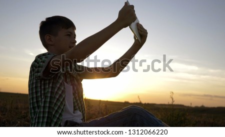 boy talking on video call on tablet sitting in field at sunset
