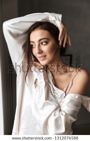 Photo of caucasian woman 20s wearing white shirt standing near window at home