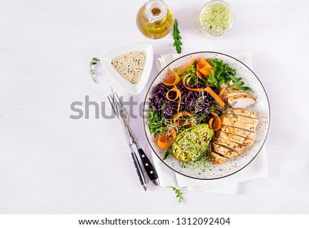 Buddha bowl dish with chicken fillet, avocado, red cabbage, carrot, fresh lettuce salad and sesame. Detox and healthy keto diet bowl concept. Overhead, top view, flat lay, copy space
