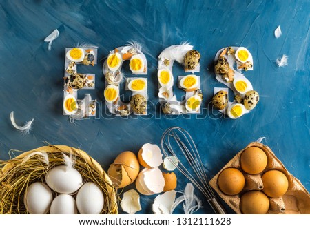 Chicken and quail eggs with word eggs on blue background with basket, feathers and box