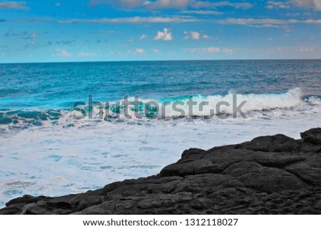 Waves breaking onto a beach of volcanic rock.