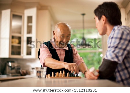 Excited senior man having fun playing chess with his grandson.