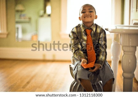 Young boy smiles and plays with his necktie as he sits on a stool in a bathroom.