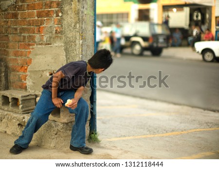 Boy sitting on a concrete brink peers around the corner of a building.