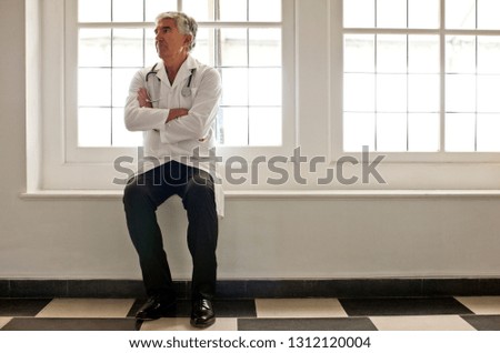 Portrait of worried looking doctor sitting in corridor.