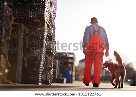 Young fisherman wearing overalls walking with his dog along a dock.