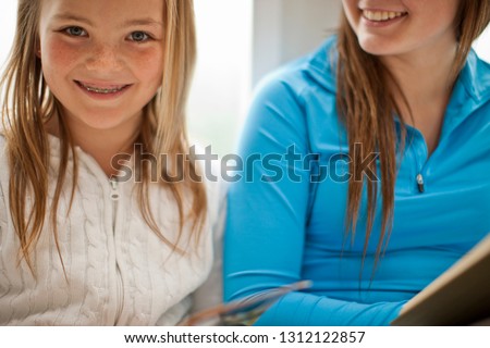 Portrait of a smiling young girl reading a book with her older sister.