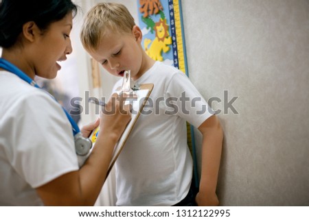 Little boy curiously looking at the nurse writing notes.
