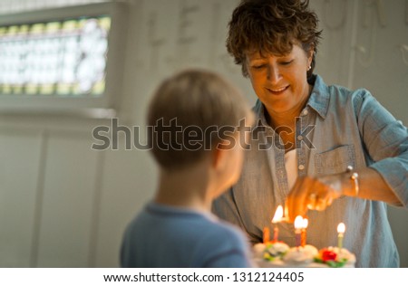 Young boy holding birthday cake while his grandmother lights the candles.