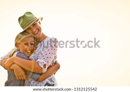 Portrait of a smiling teenage girl hugging her younger sister on a beach.