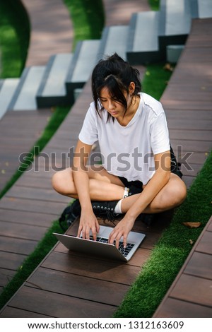Portrait of a beautiful and young Chinese Asian student girl sitting on a step on her university campus lawn and is working on her laptop computer.