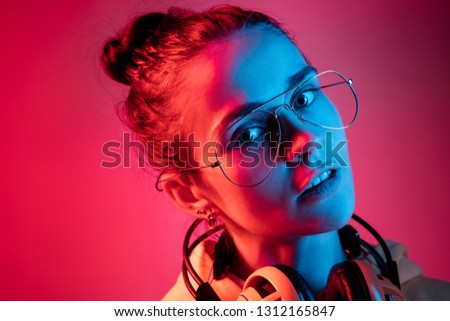 Fashion pretty woman with headphones listening to music over red neon background at studio.