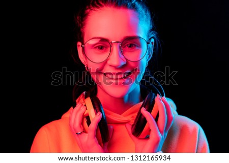 Fashion pretty woman with headphones listening to music over black neon background at studio.