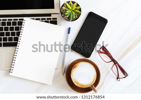 Blank white paper note book with pencil, glasses, coffee cup, mobile and laptop on desk. Business idea and technology concept.