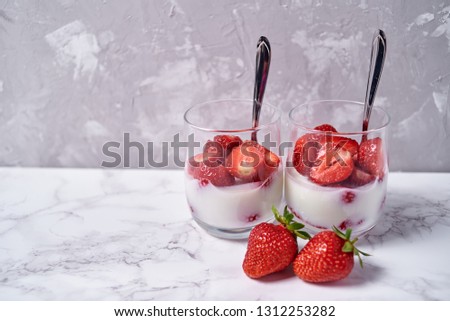 Two glasses of healthy yogurt with fresh sliced strawberry and spoons on white marble table background, copy space. Healthy breakfast, food concept