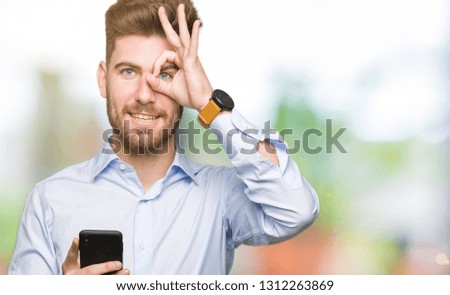 Young handsome man business using smartphone with happy face smiling doing ok sign with hand on eye looking through fingers